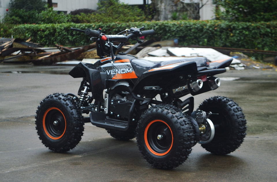 49cc Mini Quad ATV in orange/black combo parked diagonally facing its rear to the left side of ATV revealing dual exhaust pipes and free upgrade to matching orange rims