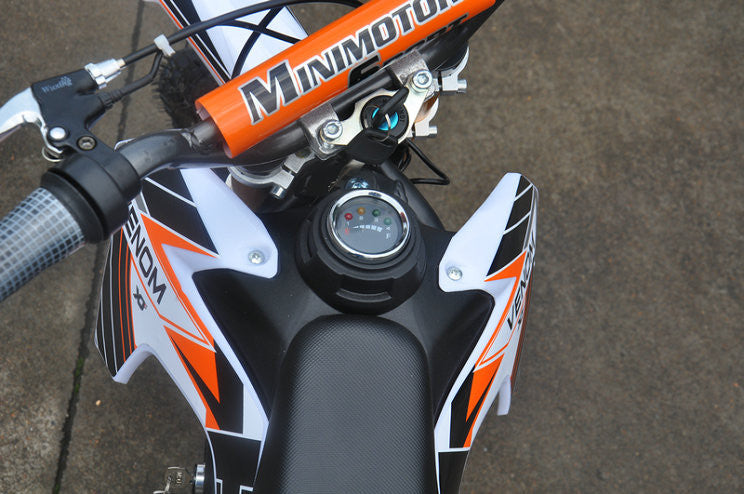Sitting down view of Orange and white fully electric dirt bike 500 watts 24 volts. Battery indiactor, key switch indicator, handle bars are revealed.